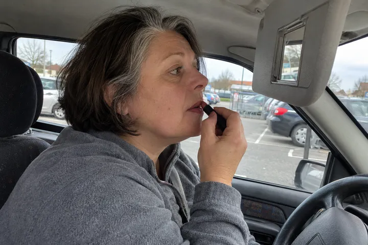 Frau zieht im Auto im Spiegel der Sonnenblende ihren Lippenstift nach