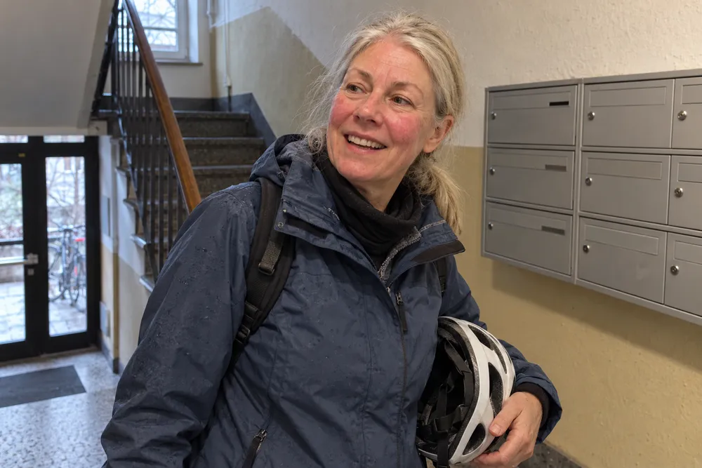 Frau kommt mit Fahrradhelm im Treppenhaus nach Hause, ihre Wangen sind von der Kälte gerötet